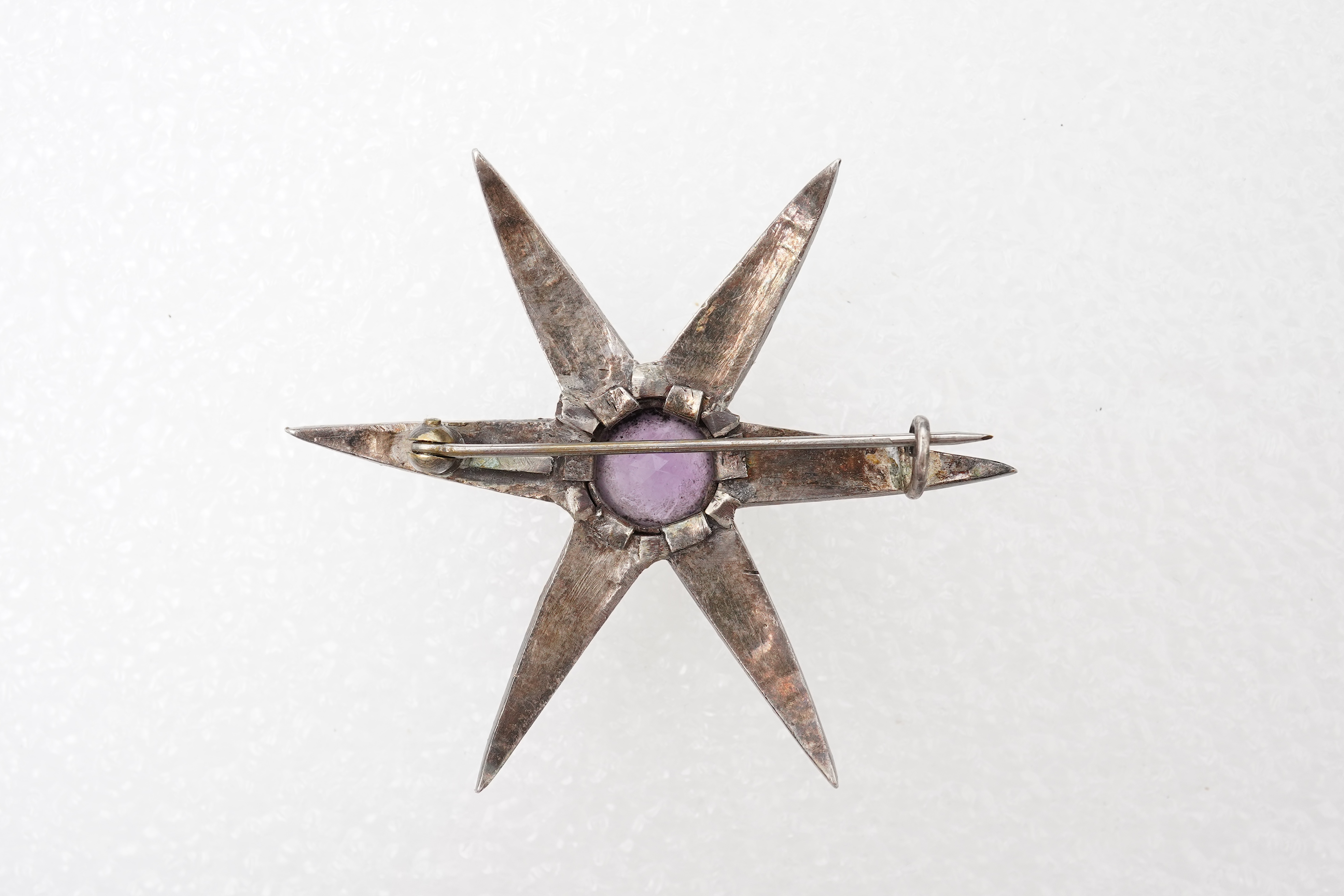 An amethyst and diamond brooch, designed as a star, set with a circular-cut amethyst and rose-cut diamonds, mounted in silver and gold, length 5.7cm, two diamonds deficient